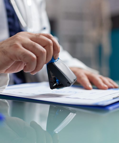 Doctor holding medical stamp to put on prescription paper Doctor holding medical stamp to put on prescription paper at health care exam. Hand of physician putting seal on checkup report, giving medicine to patient at consultation. Close up