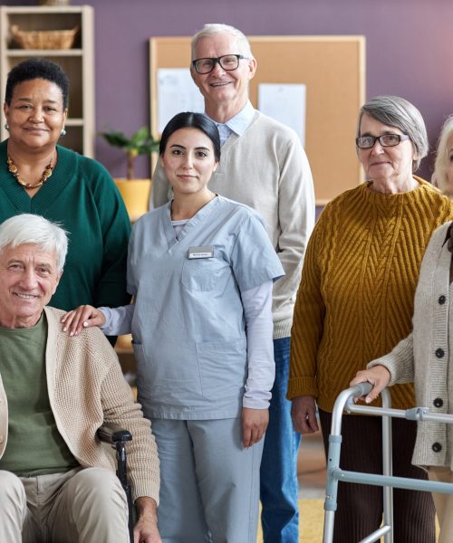 Senior people looking at camera in retirement home while posing with nurse Diverse group of senior people looking at camera in retirement home while posing with nurse all smiling